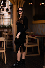 Fototapeta na wymiar Photo of brunette lady posing on wooden background in cafe.Fashion style portrait. Girl wearing dark casual dress, sunglasses and dark hat .Fashion concept.