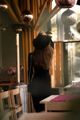 Photo of brunette lady posing on wooden background in cafe.Fashion style portrait. Girl wearing dark casual dress, sunglasses and dark hat .Fashion concept. Back view