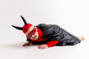 Man in devil masquerade costume and devil horns lying on white stufio background