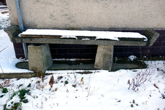 Abandoned and damaged bench covered with snow in winter near the building
