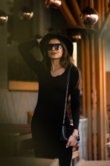 Obraz na płótnie Canvas Photo of brunette lady posing on wooden background in cafe.Fashion style portrait. Girl wearing dark casual dress, sunglasses and dark hat .Fashion concept.