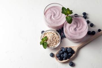 two fresh blueberry yogurt with blueberries and cereals on a white texture table, ingredients for cooking, top view, copy space