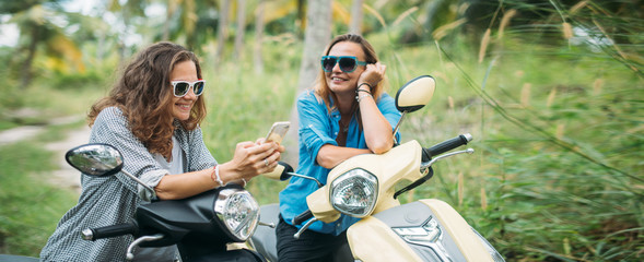 A pair of beautiful women travel by scooter through the jungle in Southeast Asia. Phone navigation