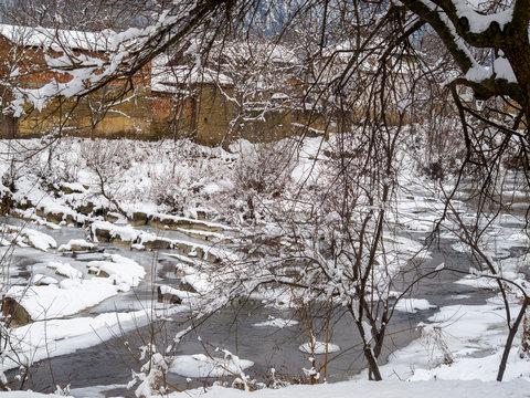 Picturesque snowy rural view of the winter Vidima River with riverbank houses through covered with snow winter vegetation at the Bulgarian Fore-Balkan village of Debnevo, Central-North Bulgaria