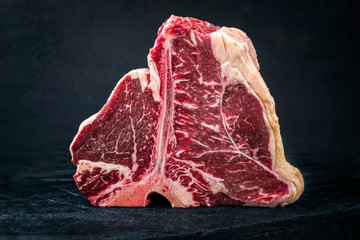 Raw dry aged wagyu porterhouse beef steak with large fillet piece as closeup on a black burnt...