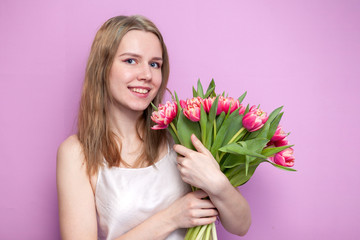 young beautiful girl with a bouquet of flowers on a colored pink background, a woman holds tulips and smiles