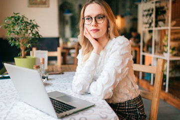 Beautiful young freelancer woman using laptop computer sitting at cafe table. Happy smiling girl working online or studying and learning while using notebook. Freelance work, business people concept