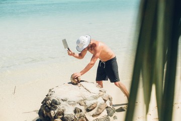 man cuts open coconut with a machete on a tropical beach