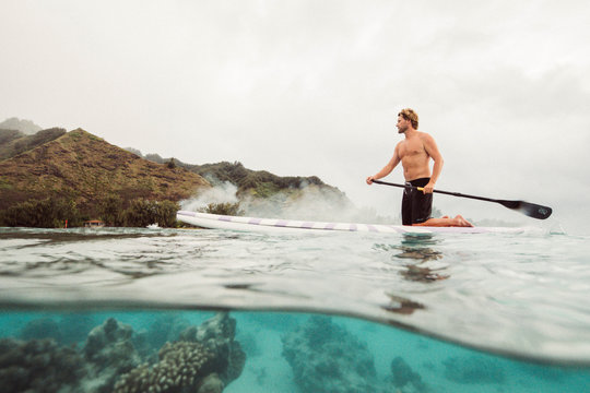 man paddle boards over tropical coral reef on a misty day
