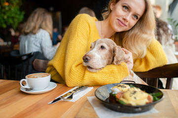 Young caucasian cheerful blonde girl sitting and hugging together with her lovely cocker spaniel...