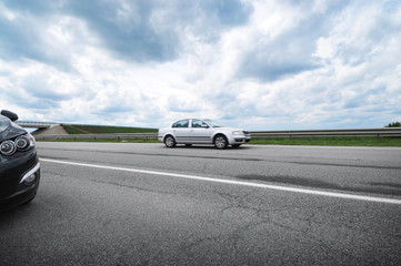 Fototapeta premium Cars on the countryside road against a cloudy sky