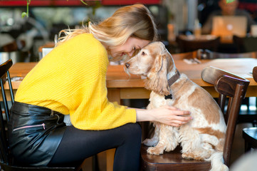 Caucasian young blonde girl siiting in caffe on chair face to face to her beloved cocker spaniel...