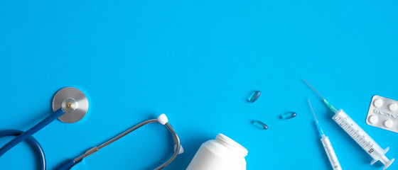 Medical equipment banner with stethoscope, pills, syringe on blue background. Flat lay, top view. Healthcare and medical concept.