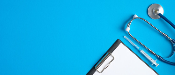 Pediatric equipment on blue background. Top view medical clipboard, stethoscope and syringe. Medical banner template with copy space, header mockup. Healthcare and medical concept.