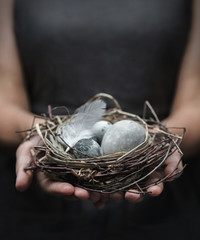 Woman hands holding marble Easter eggs with feathers on dark background. Happy Easter holiday, selective focus