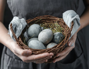 Woman hands holding wicker basket with Easter eggs on dark background. Happy Easter holiday, selective focus