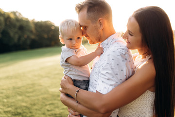 Sensual photo of a happy family. Parents gently hug their little beloved baby son, outdoors at the sunset