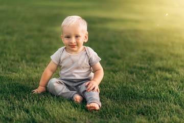 Adorable baby boy with blue eyes sits on the grass and smiles. Copy space