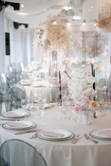 Decor of a wedding luxury dinner in white and pink colors. Served tables with silver and gold objects, plates, glasses and cutlery. Fresh flowers roses in vases.