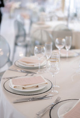 Decor of a wedding luxury dinner in white and pink colors. Served tables with silver and gold objects, plates, glasses and cutlery.