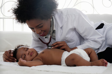 african american doctor examining black baby boy sleeping on bed with stethoscope