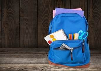 Colorful school supplies in a backpack on wooden background
