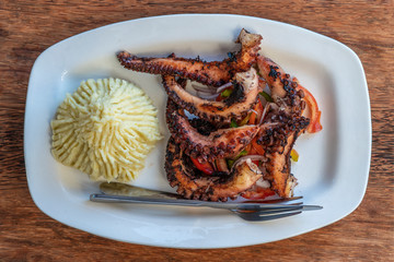 Fried octopus tentacles with mashed potato and vegetable salad on a white plate, close up
