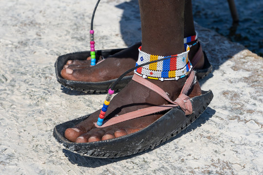 Tribal Masai Legs With A Colorful Bracelet And Sandals Made Of Car Tires, Close Up. Island Of Zanzibar, Tanzania, Africa