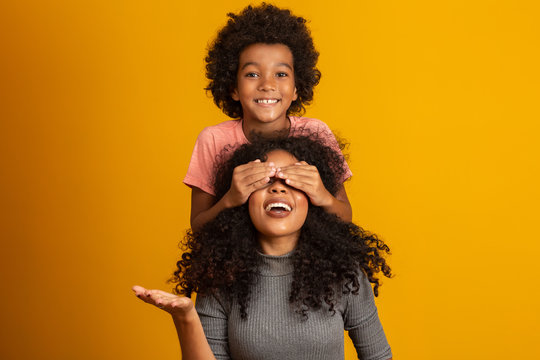 African American boy holding his mother closed eyes. Yellow background. Mothers Day. Brazilian family.