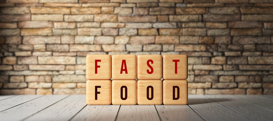 cubes with message FAST FOOD on wooden floor in front of a brick wall