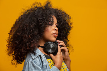 People, music, emotions concept. Delighted carefree female with Afro hairstyle dances in rhythm of melody, closes eyes listens loud song in headphones. Beautiful afro woman with her headphones