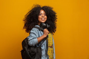 Female student in campus with books in her arms. Yellow background.