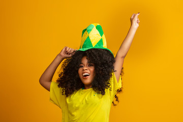 Brazil supporter. Brazilian woman fan celebrating on soccer or football match on yellow background. Brazil colors.