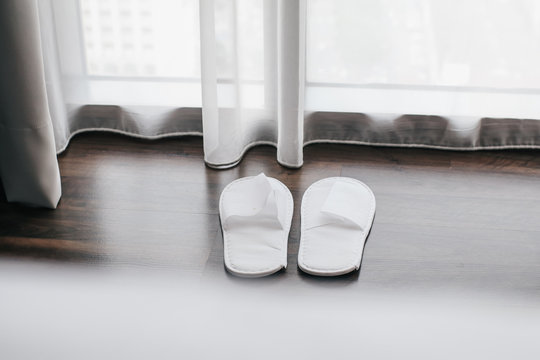 White slippers by the window with see through sheer curtain and soft sunlight on wooden floor, Modern room interior relax and vacation concept