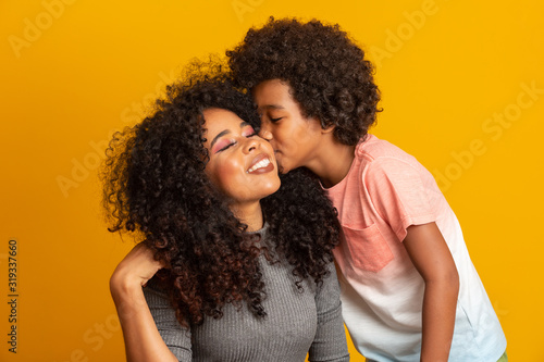 Portrait of young African American mother with toddler son. Son kissing his mother. Yellow background. Brazilian family.