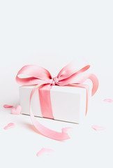 White gift box with pink ribbon and a small pink hearts on white background. Selective focus. Copy space