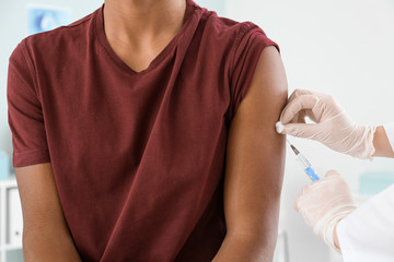 Doctor vaccinating teenage boy in clinic, closeup