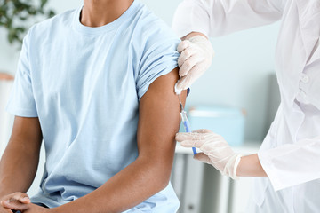 Doctor vaccinating teenage boy in clinic, closeup