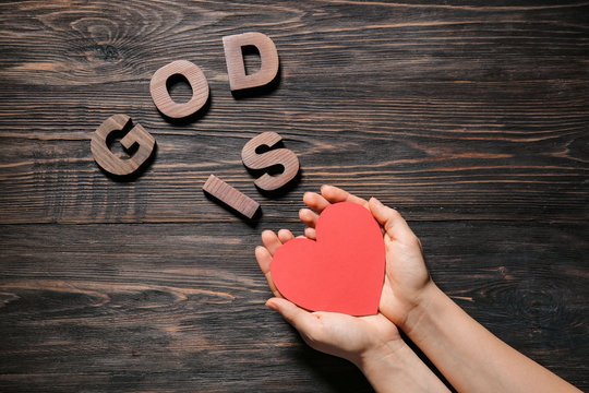 Female hands and text GOD IS LOVE on wooden background