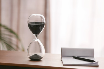 Hourglass with notebook on table in office. Time management concept
