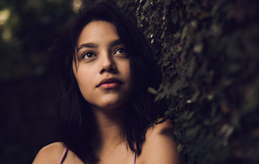 Beautiful and attractive young woman with contemplative look leaning against a wall with natural grass, young woman thinking about life