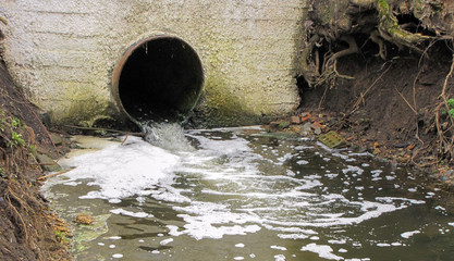 Discharge of untreated water into a natural lake. Bad, dirty, untreated water flows from a pipe. Environmental pollution by wastewater.
