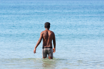 Fototapeta na wymiar A dark skinned athletic guy enters the water