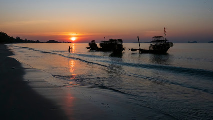 Fototapeta premium Silhouette of a traditional Thai fishing boat with a background of the golden glow of sunrise and the reflections of the rising sun on the water.