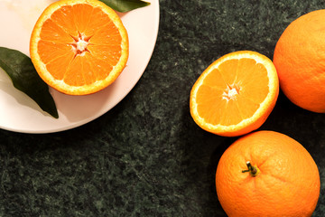 Oranges and Orange Slices on white plate with leafs on green marble.