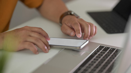 Side view of male freelancer typing on smartphone in workspace with laptop and office supplies