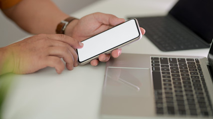 Side view of male freelancer using smartphone in workspace with laptop and tablet on white table