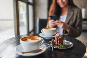 Closeup image of an asian woman holding and using mobile phone with coffee cup and snack on the table in cafe