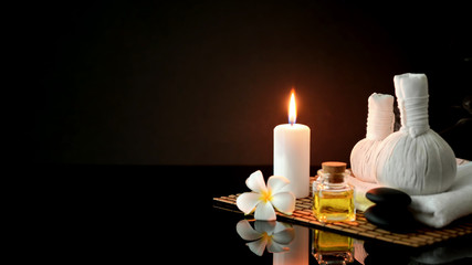 Cropped shot of spa treatment accessories with white towel, candle and aroma oil on dark background