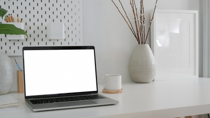 Cropped shot of modern workspace with blank screen laptop, mock up frame and ceramic vase on white table